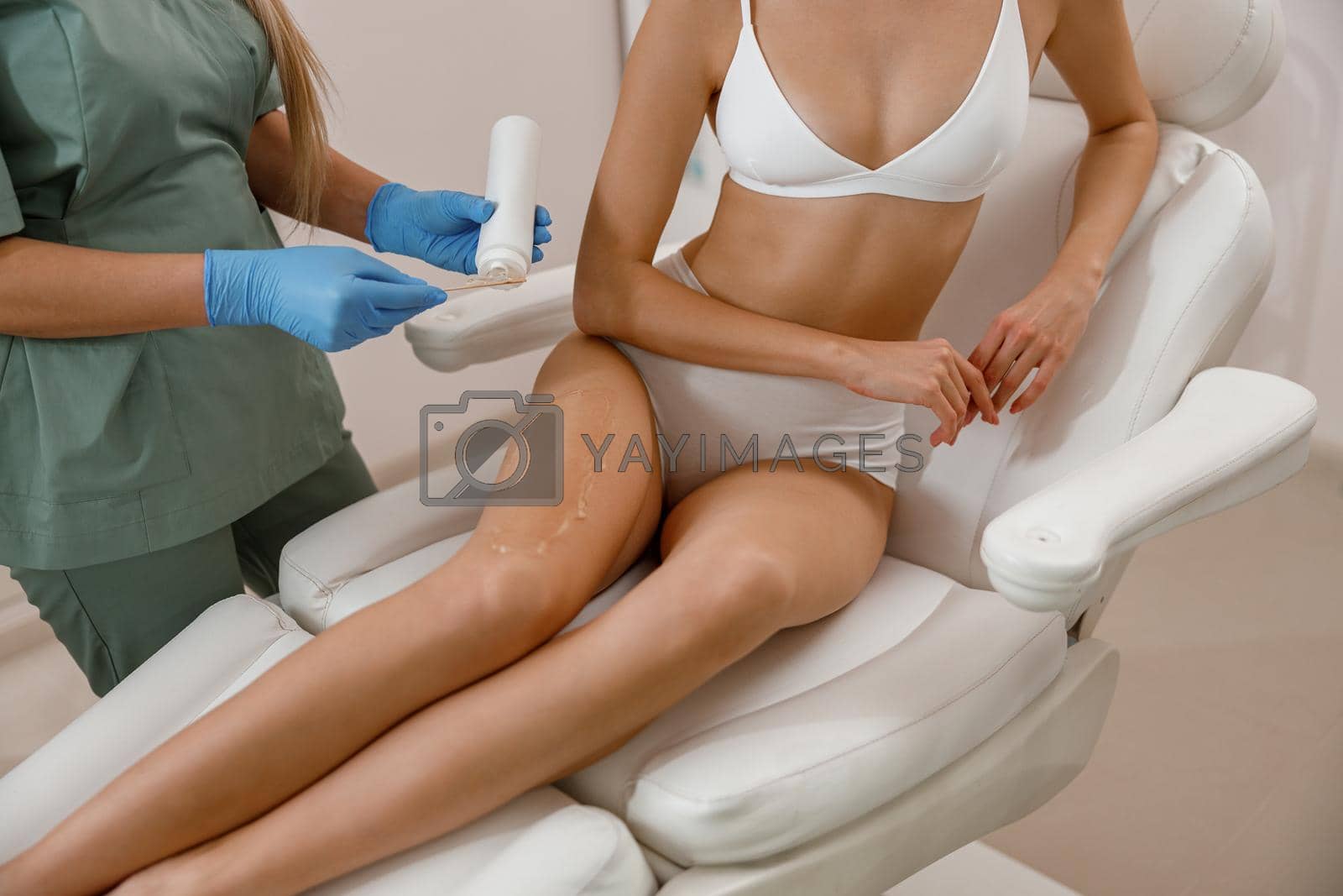 Cosmetologist applying ointment on client legs before photo epilation procedure. Hair removal