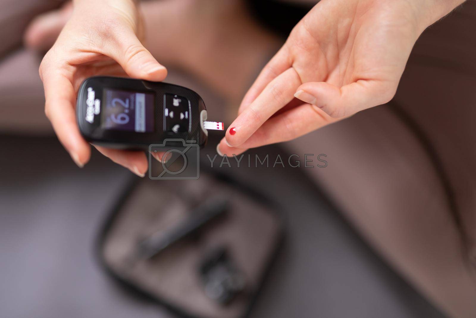 Royalty free image of Blood sugar testing at home. Woman checking blood sugar level by glucometer and test stripe at home. Diabetic checking blood sugar levels. by kasto