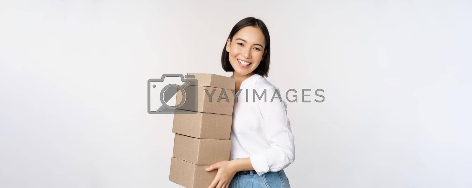 Royalty free image of Portrait of young asian woman holding boxes, carry delivery goods. Korean female entrepreneur assemble order, standing voer white background by Benzoix