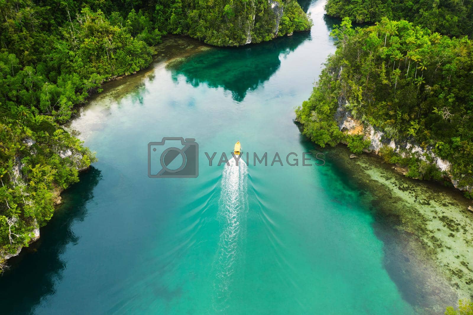 High angle shot of a boat sailing through a canal running along the Raja Ampat Islands in Indonesia.