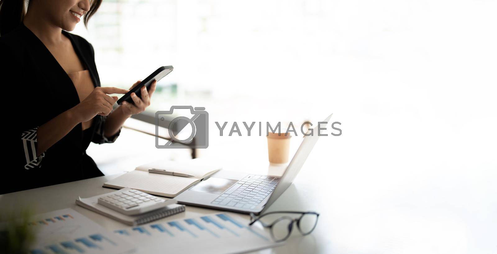 Royalty free image of Asian woman holding smart phone while using calculator for business financial accounting calculate money bank loan rent payments manage expenses finances taxes doing paperwork concept, close up. by nateemee