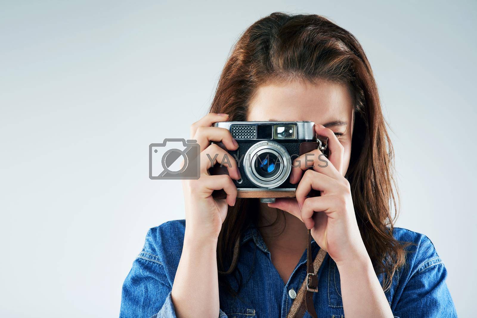 Royalty free image of Retro is the way to go. Studio portrait of a young woman using a vintage camera against a grey background. by YuriArcurs