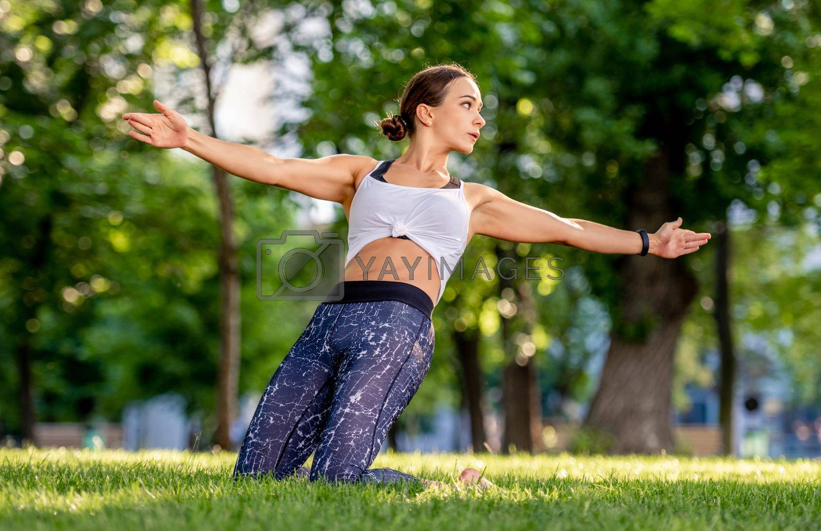 Girl doing yoga at nature and training her balance. Young woman exercising and stertching in summertime