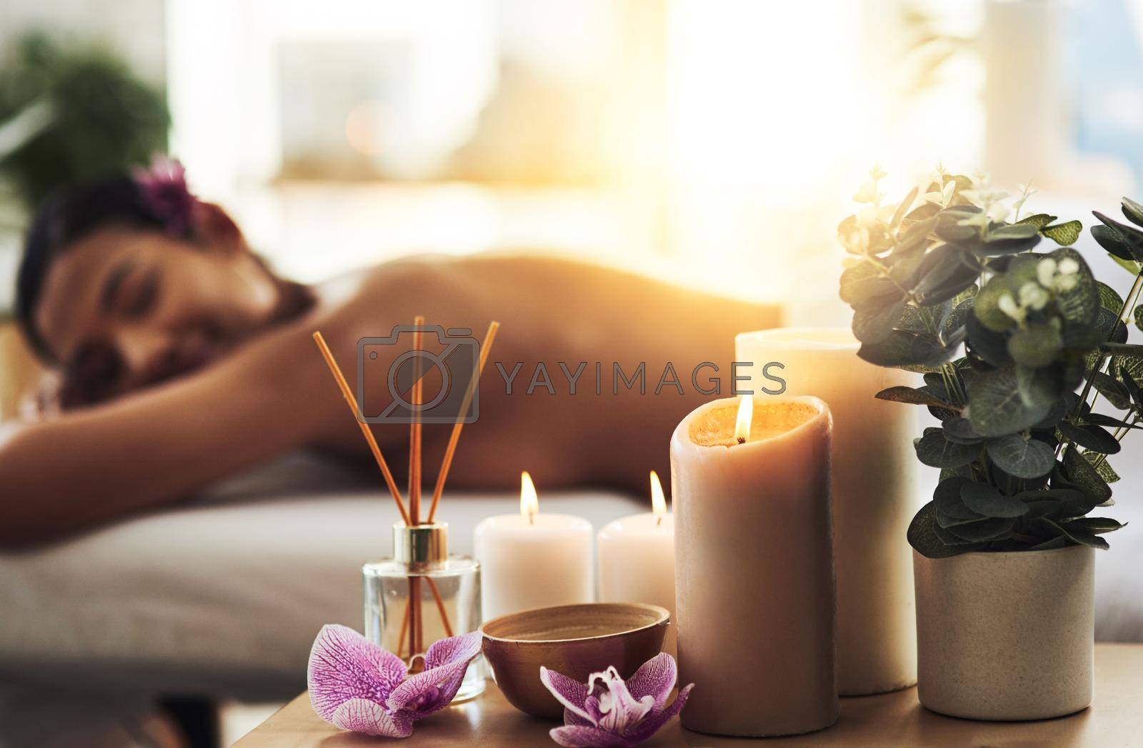 Shot of spa essentials on a table with a woman getting a massage in the background.