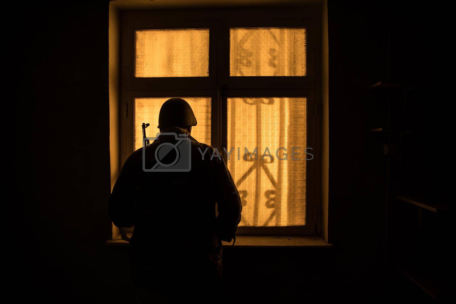 Conceptual photo of war between Russia and Ukraine. Silhouette of soldier at window at night. Old creepy room with window. Explosion outside.