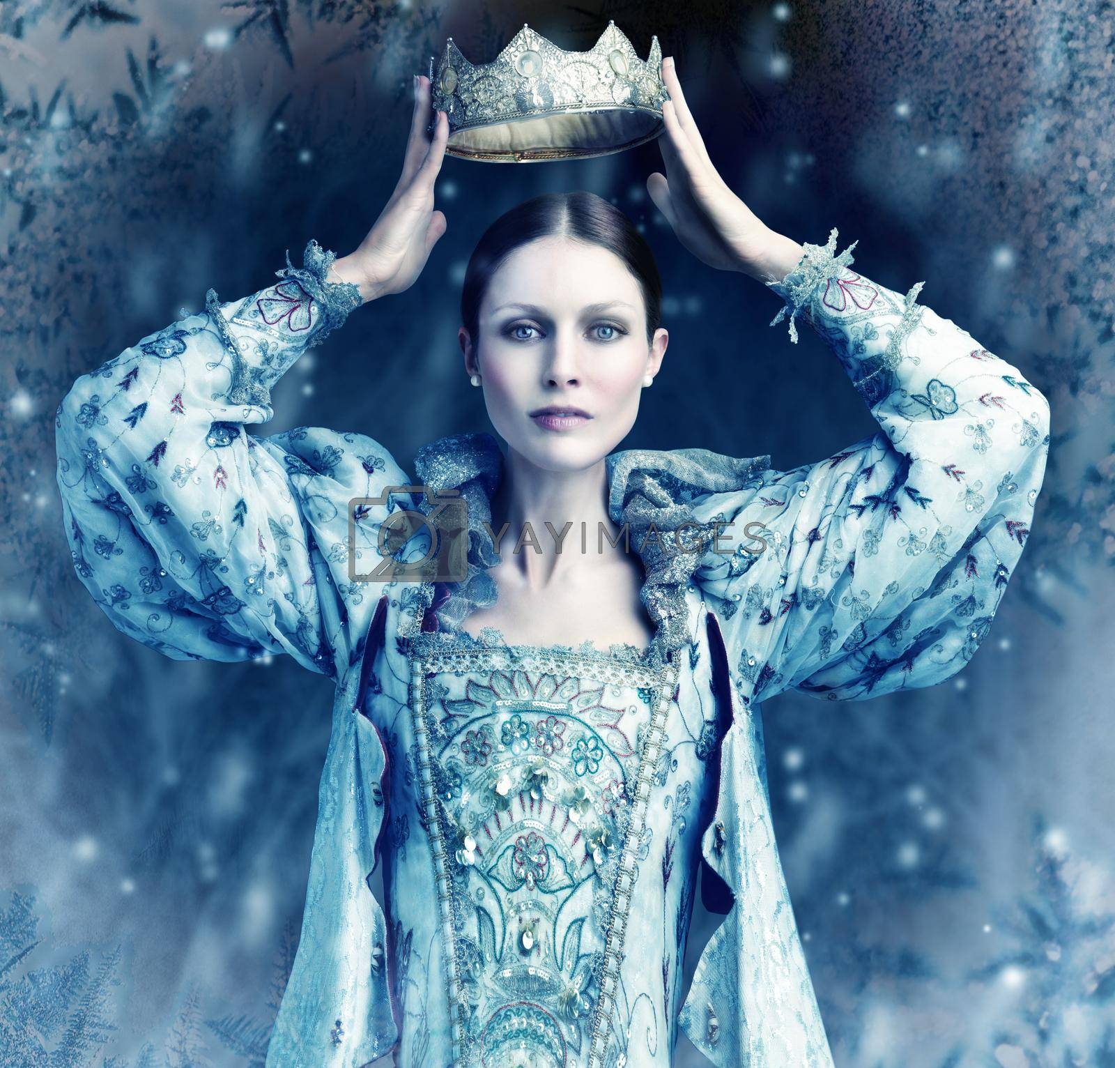 Royalty free image of The ice queen cometh. Shot of queen holding a crown over her head with snow falling around her. by YuriArcurs