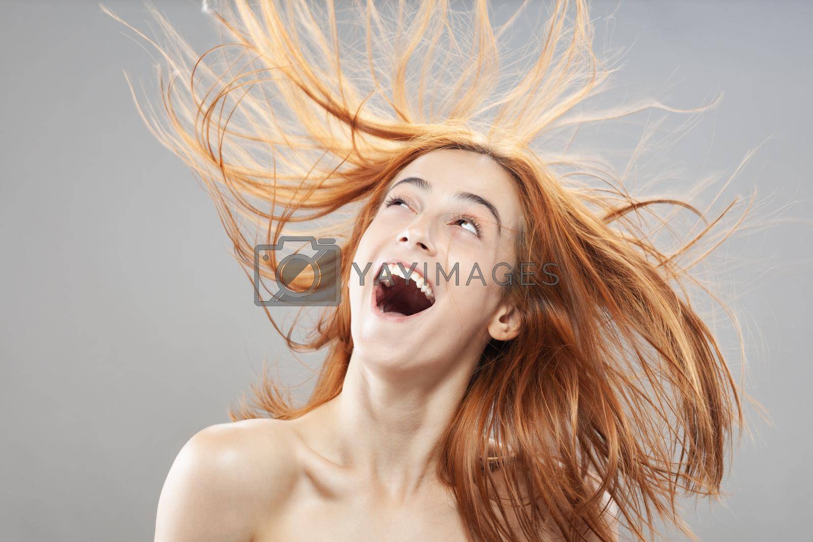 Royalty free image of Beautiful dark burnt orange windy hair girl smiling. Studio portrait with happy face expression against gray background... by kokimk