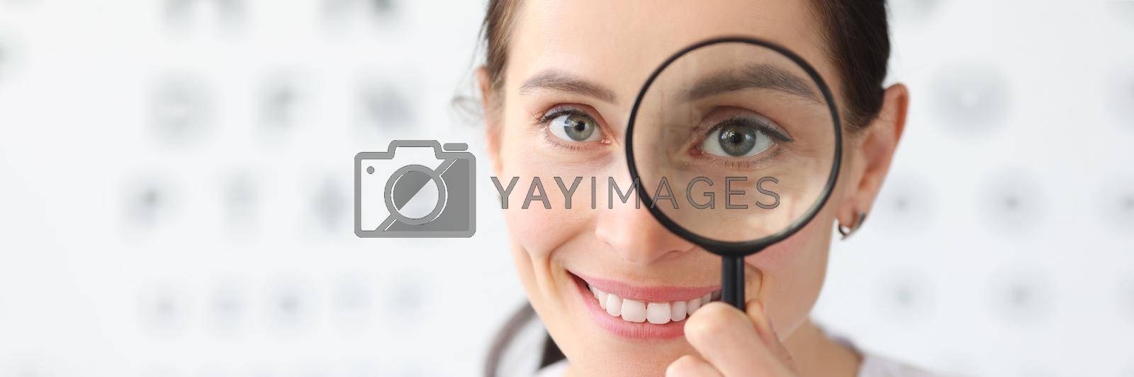 Royalty free image of Woman optometrist holding magnifying glass in eyes against background of vision examination table by kuprevich