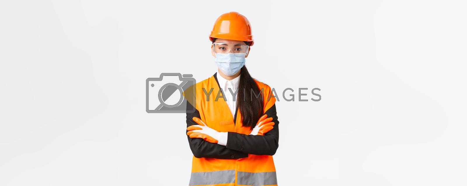 Royalty free image of Covid-19 safety protocol at enterpise, construction and preventing virus concept. Confident asian female chief engineer looking how workers follow protocol during coronavirus, wear face mask by Benzoix
