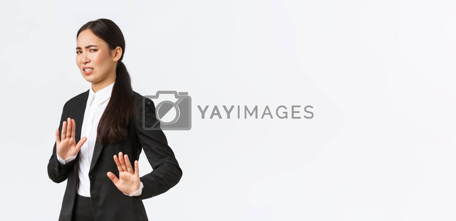 Royalty free image of Displeased asian businesswoman avoiding risky suggestions, shaking hands in refusal, rejecting disgusting strange offer. Saleswoman grimacing from aversion and step away, white background by Benzoix