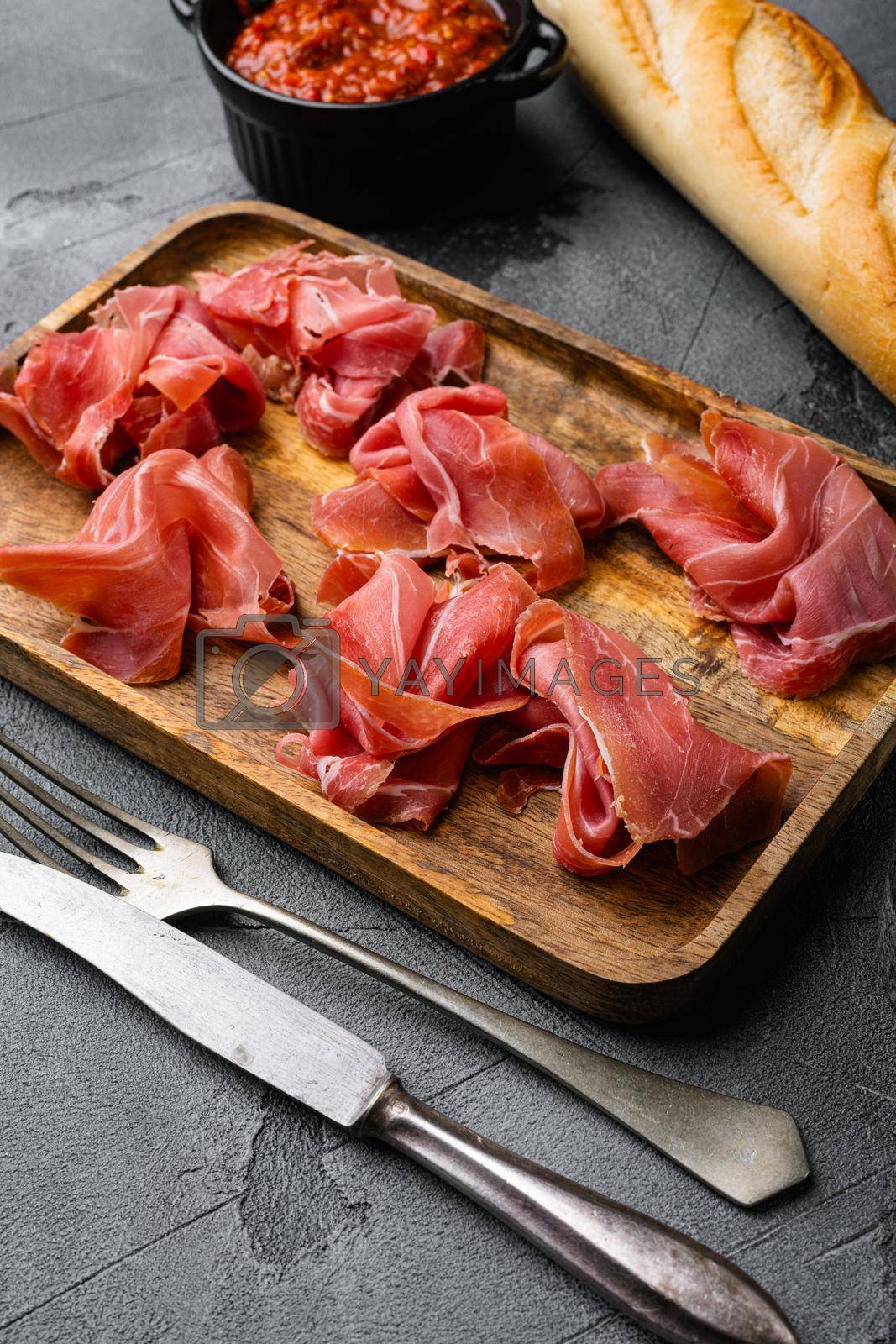 Royalty free image of Slices of prosciutto di parma or jamon serrano set, on gray stone table background by Ilianesolenyi