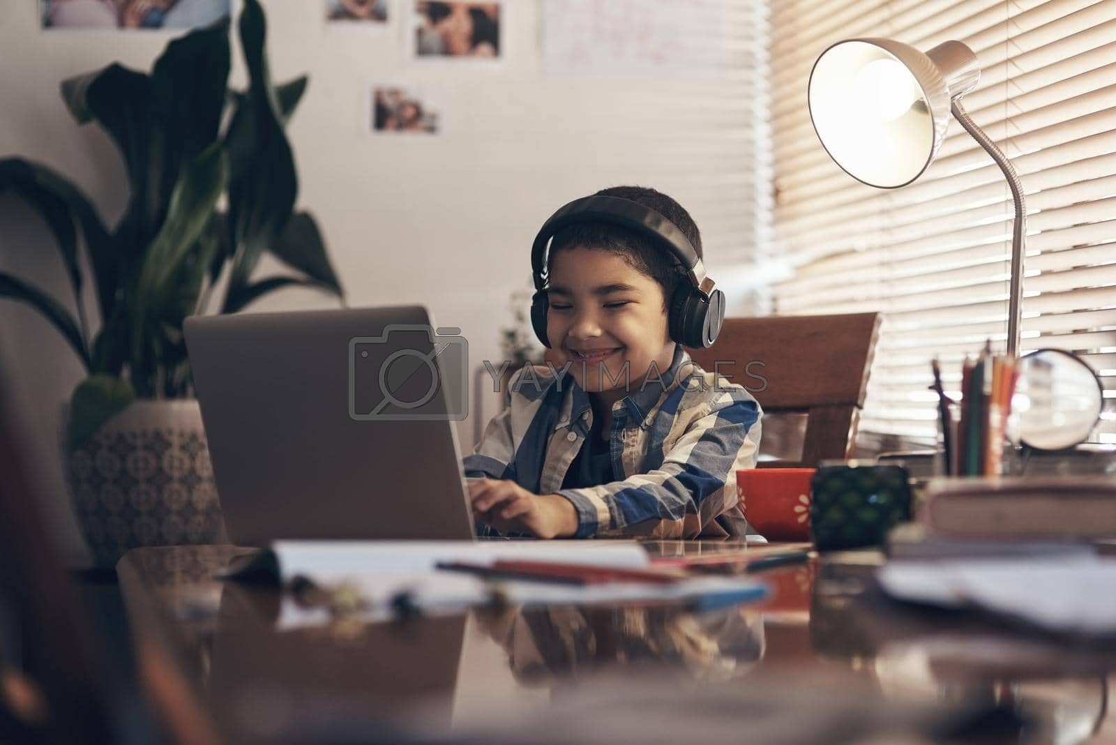 Royalty free image of Stay at home, stay in school. Shot of an adorable little boy using a laptop and headphones while completing a school assignment at home. by YuriArcurs