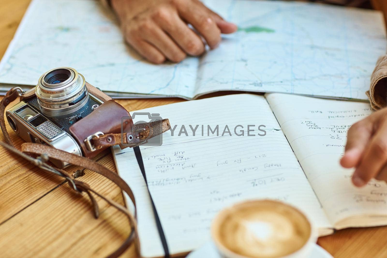 Shot of an unidentifiable tourist looking at maps and travel journals while enjoying coffee at a cafe.