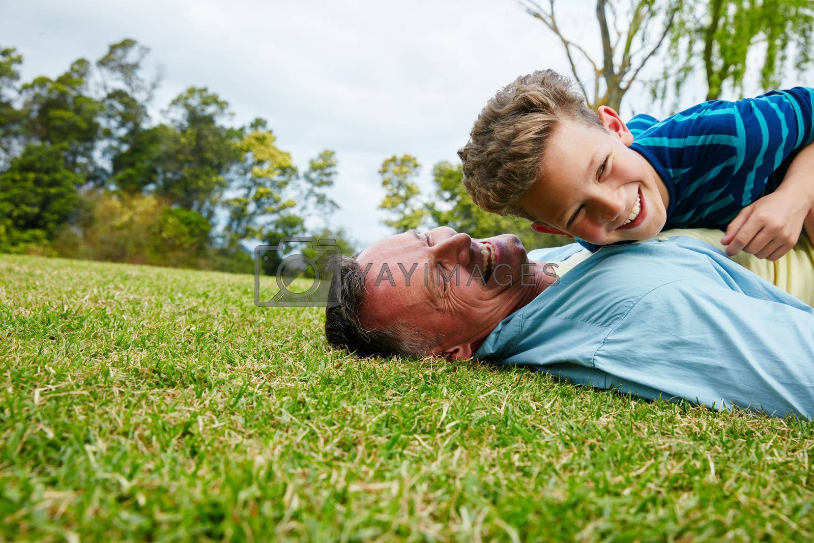 Shot of a laughing father and son lying on grass.