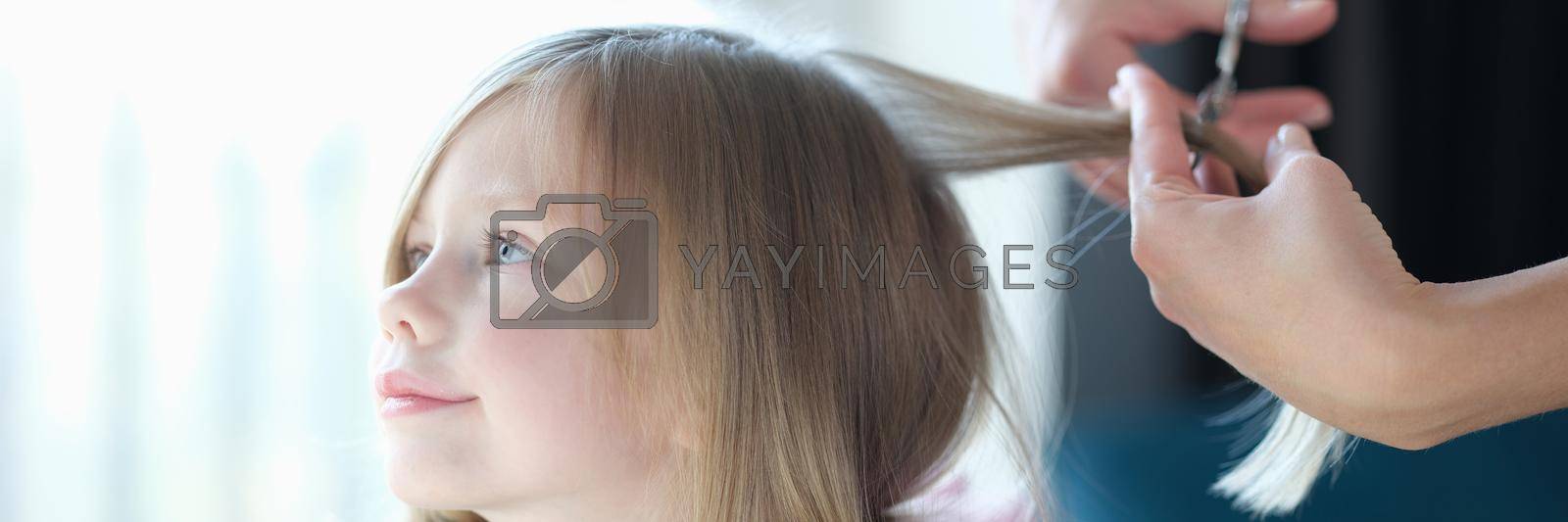Hairdresser cutting hair of little girl in beauty salon. Hairdressing services for children concept