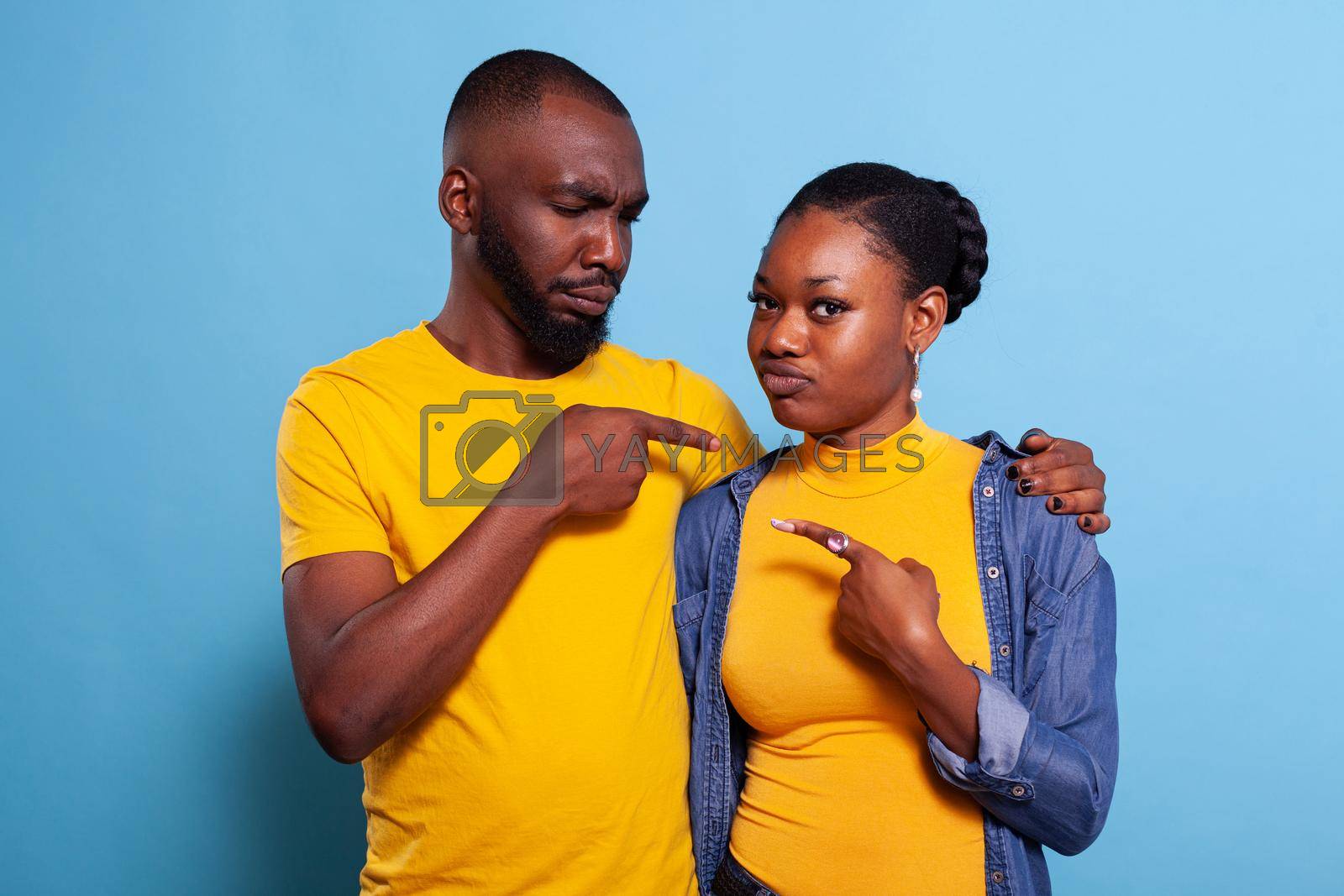 African american people pointing index fingers at each other in studio. Playful couple showing sideways directions and sharing embrace in front of camera. Romantic partners in relationship