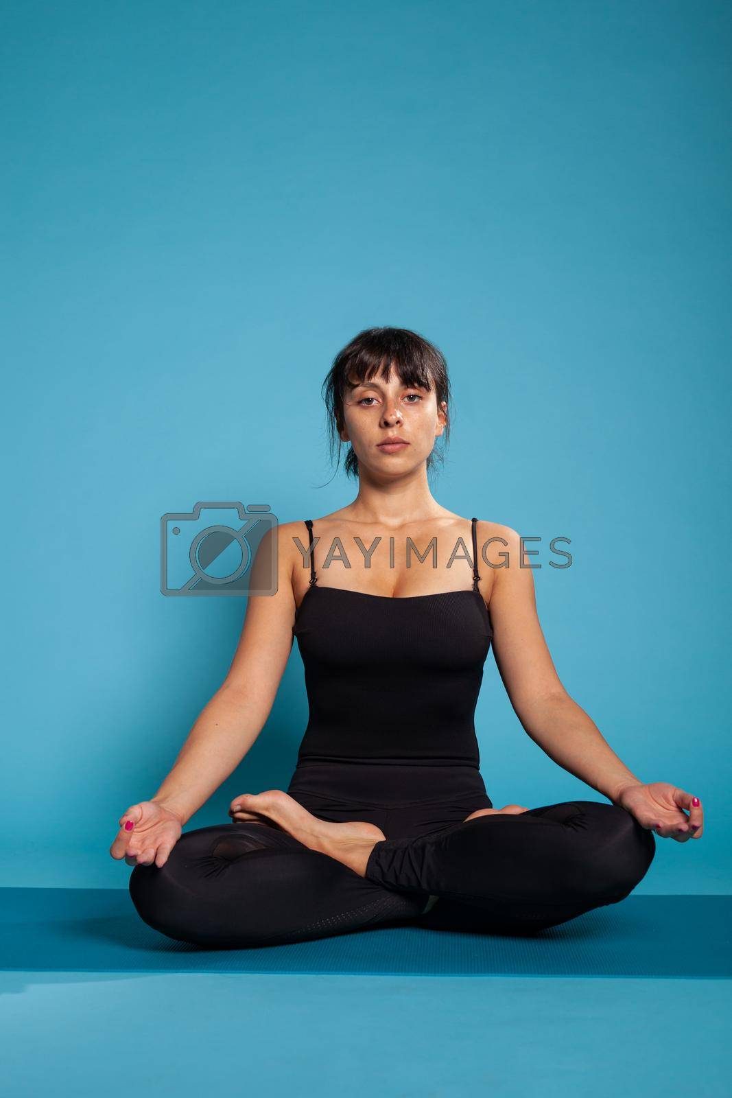 Personal trainer sitting on yoga mat in lotus position meditating during fitness workout. Athlete woman working at body posture practicing spiritual meditation. Concept of fitness exercise