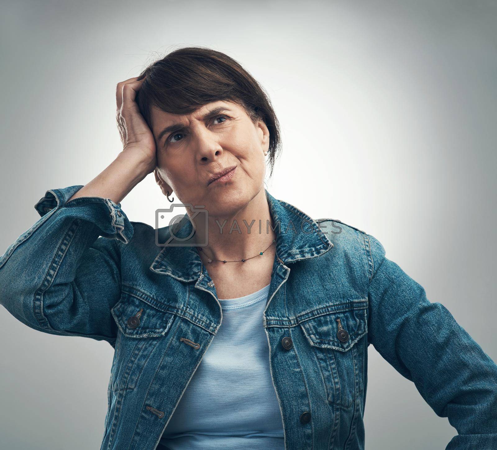 Studio shot of a senior woman scratching her head in confusion against a grey background.