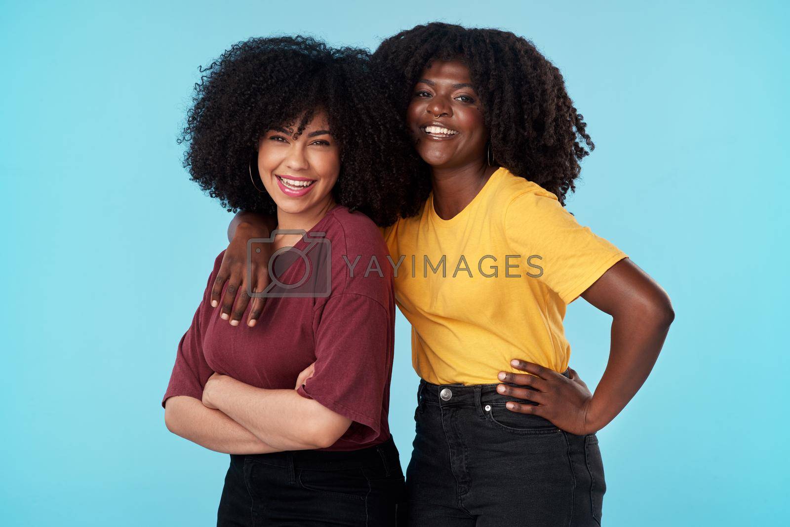 Studio shot of two young women embracing each other against a blue background.