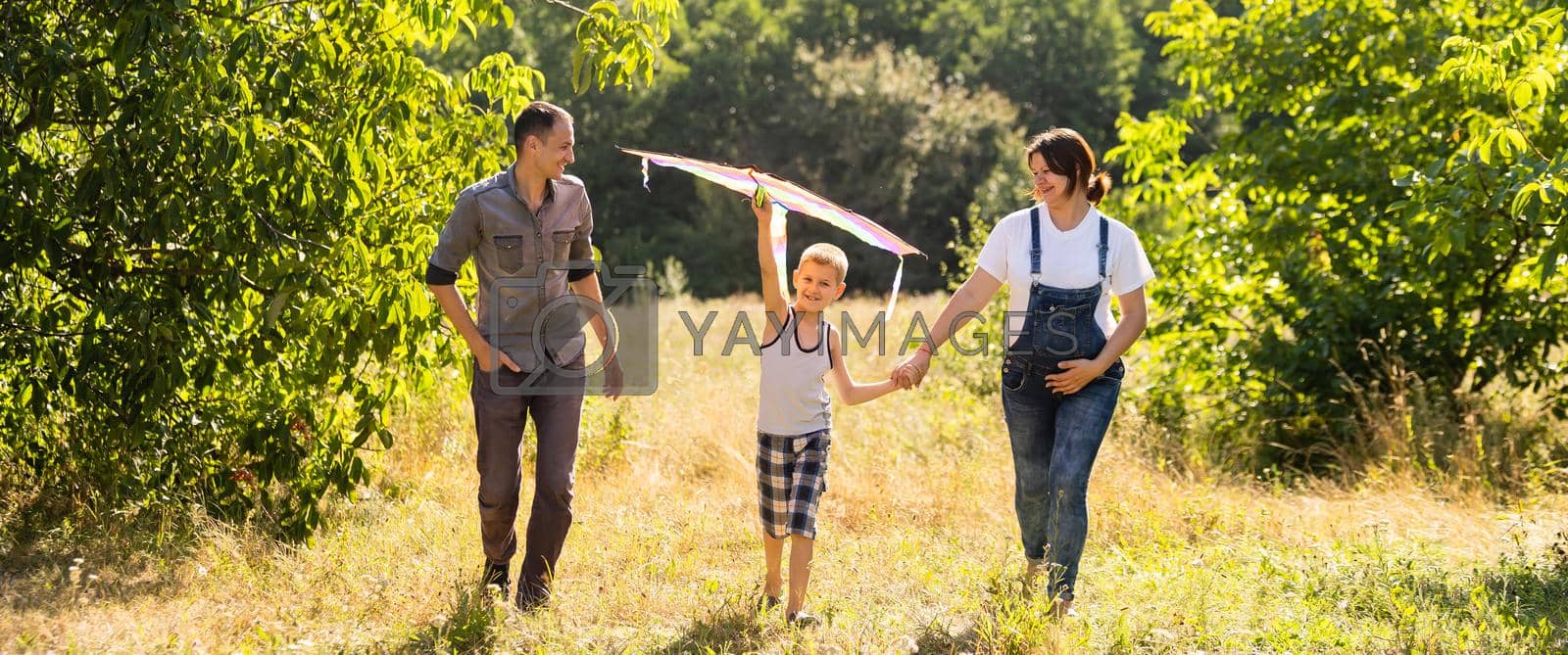 Happy family with pregnant wife fly a kite together in summer field