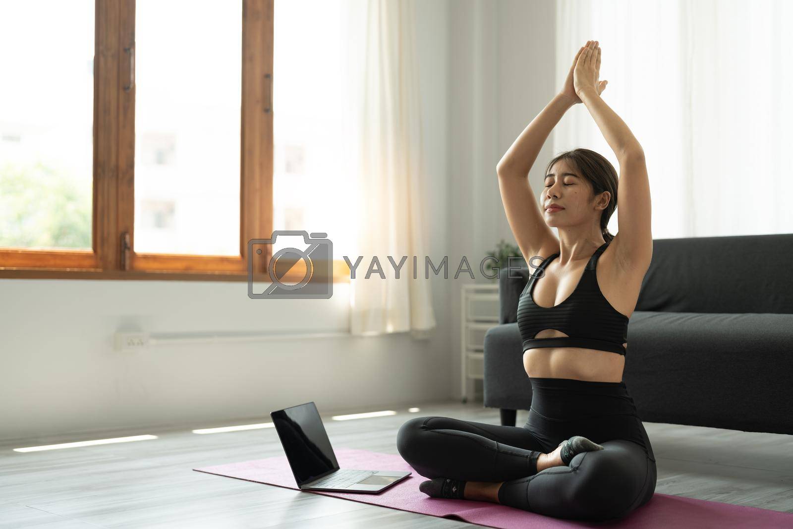 Calm relaxed young asian woman sitting in lotus position with hands up namaste gesture, closed eyes, breathing, resting, deeply meditating, practicing yoga on yoga mat at home