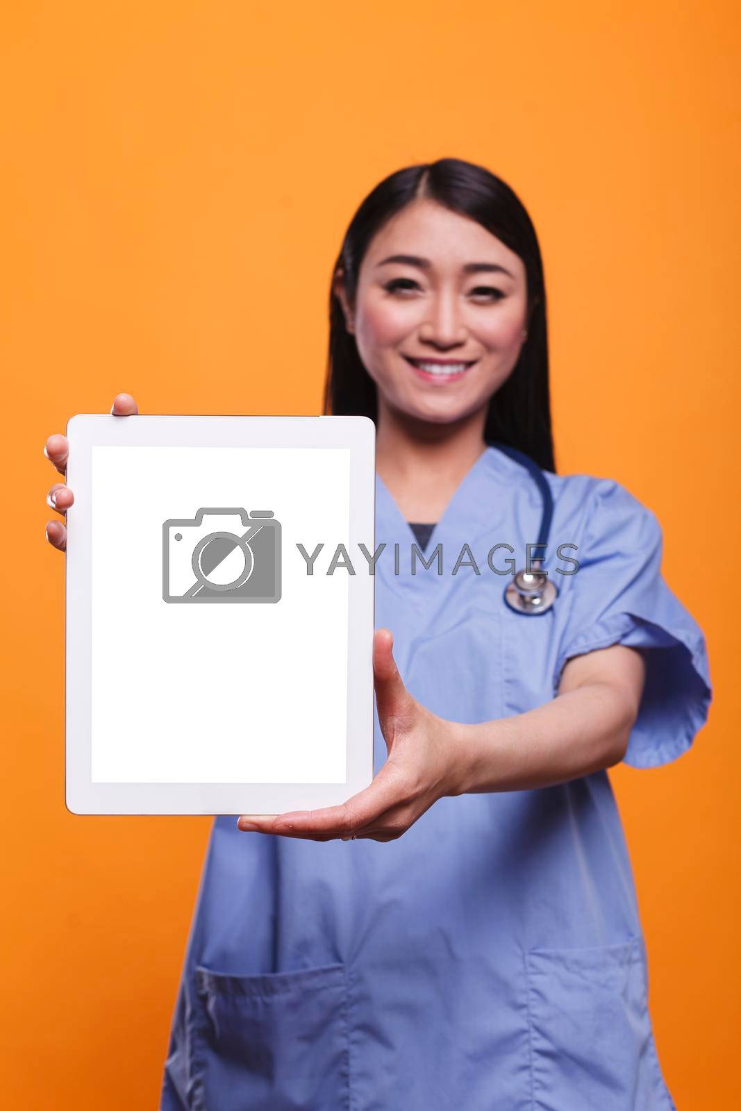 Hospital healthcare staff woman wearing stethoscope and holding digital tablet. Beautiful clinic nurse wearing stethoscope and holding modern tablet on orange background.