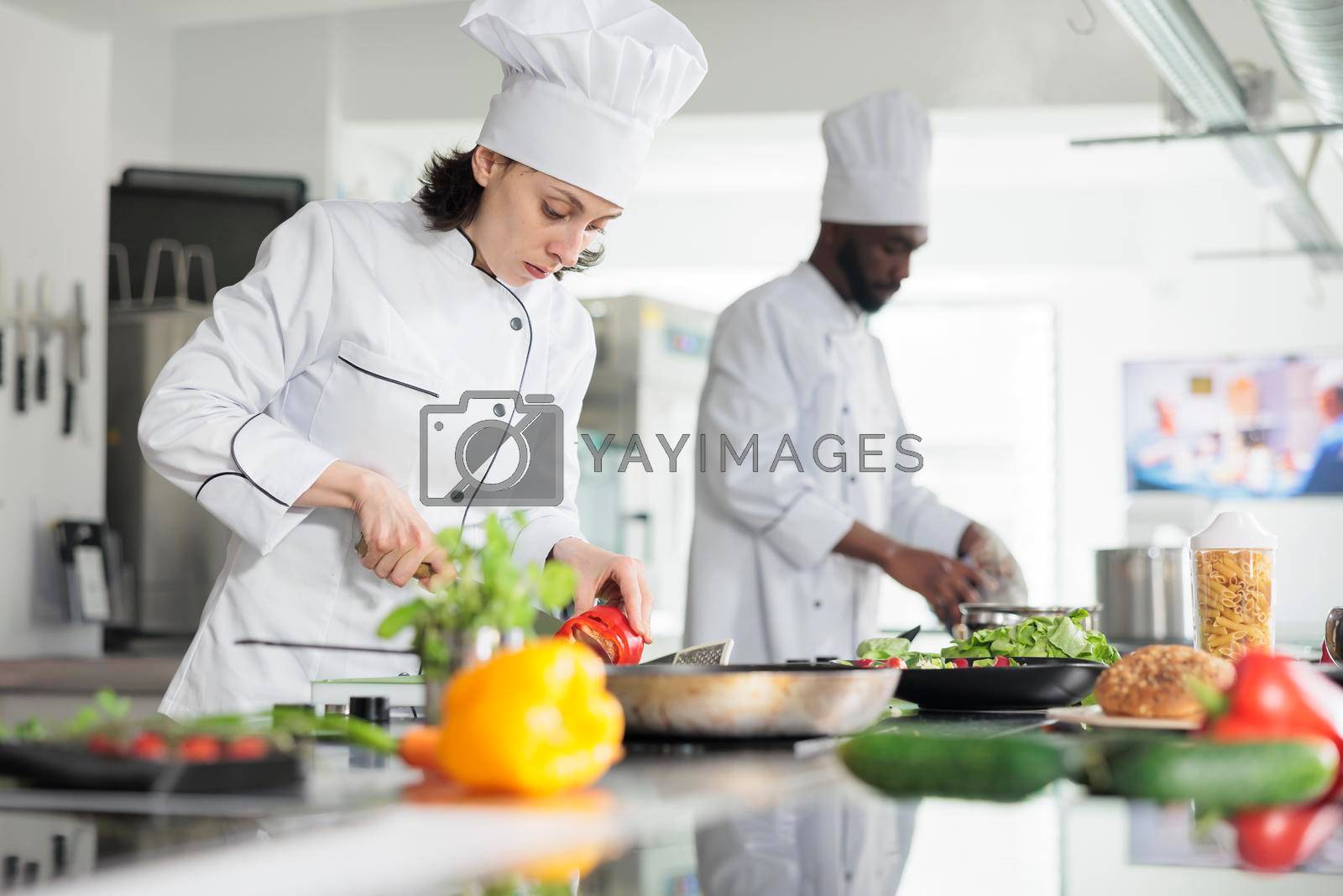 Head cook in professional kitchen cooking organic food while cutting fresh vegetables. Sous chef chopping red pepper vegetable for gourmet dish served at dinner in restaurant