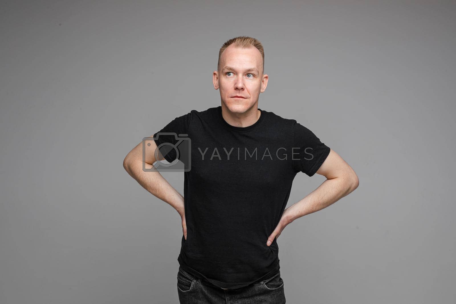 Royalty free image of attractive man with short fair hair wearing a black t-shirt and jeans keeps hands on the belt by StudioLucky