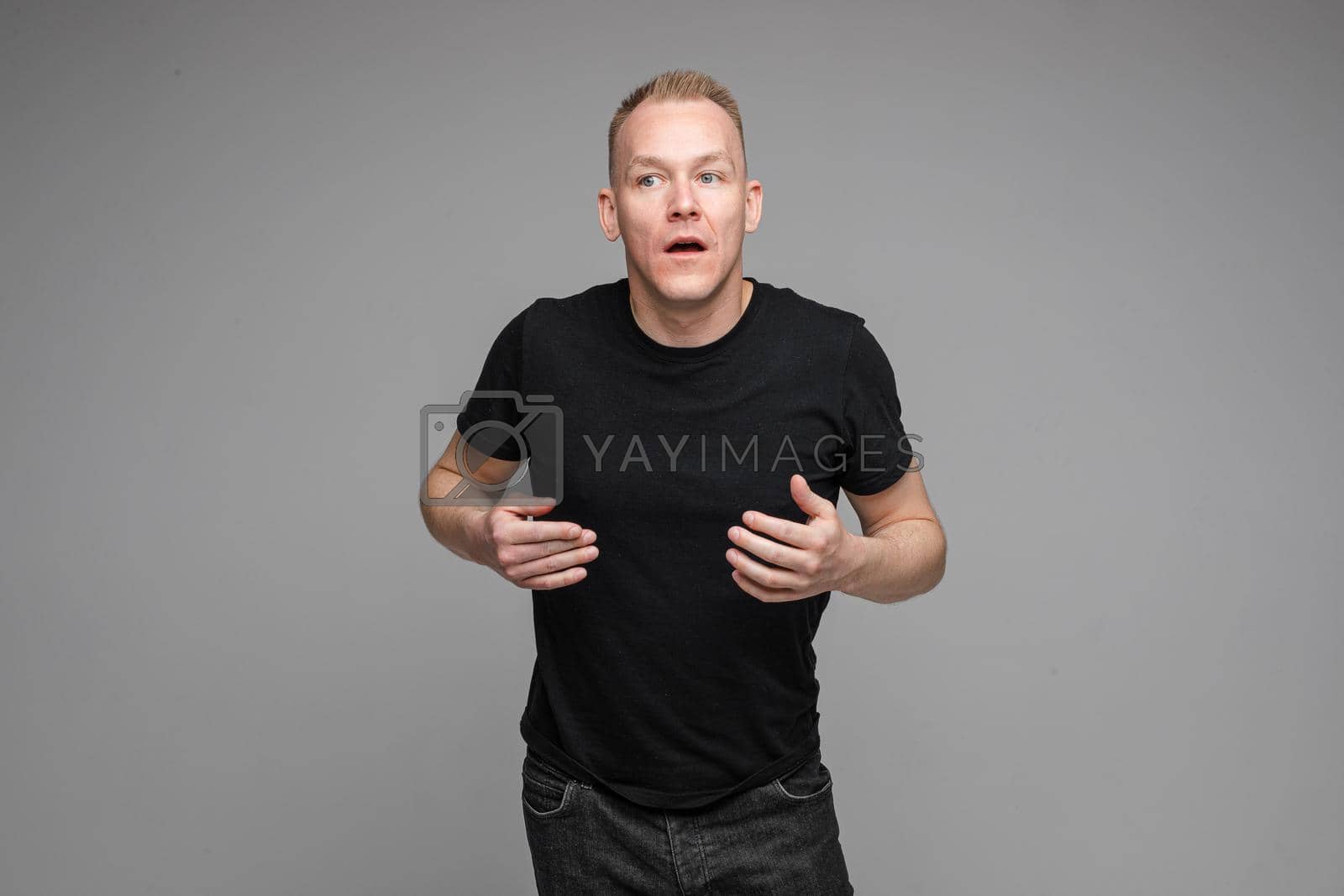 Royalty free image of strong caucasian man with short fair hair wearing a black t-shirt and jeans tries to explain something by StudioLucky