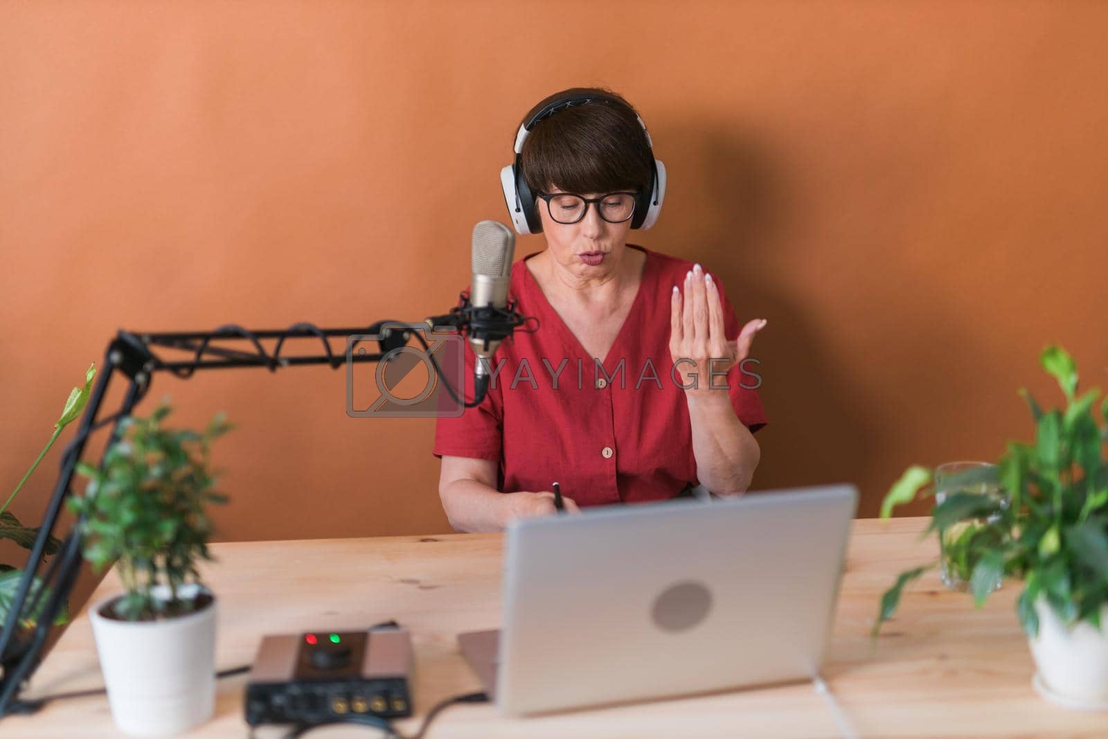 Royalty free image of Middle-aged female radio presenter talking into the microphone and reading news - radio broadcast online concept by Satura86