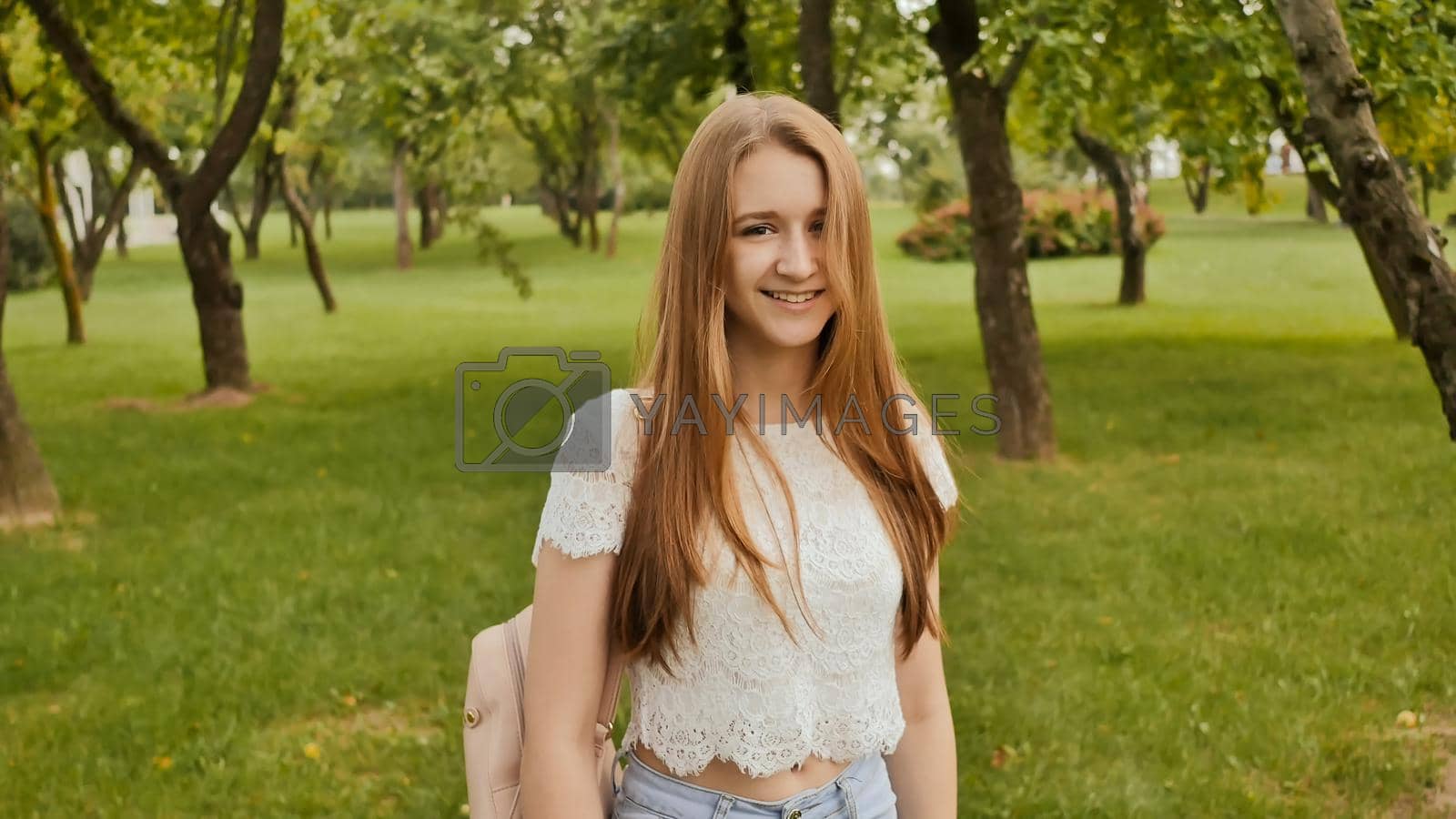 Royalty free image of Young beautiful female student with long hair with a backpack on her back is walking in the park. Rest during study. by DovidPro