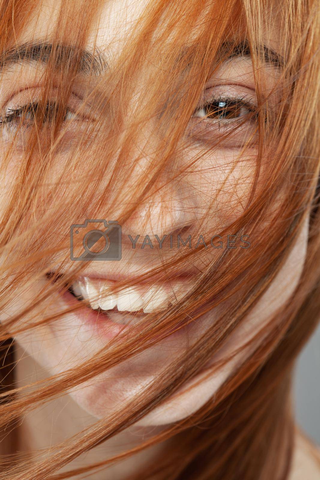Royalty free image of Beautiful dark burnt orange windy hair girl smiling. Studio portrait with happy face expression against gray background... by kokimk