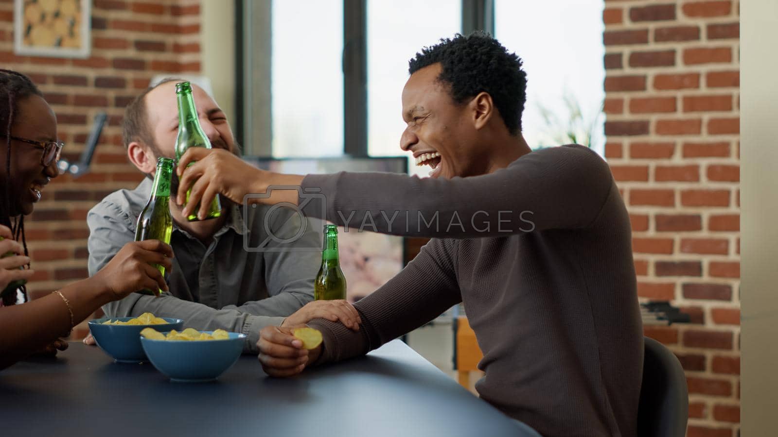 Modern group of friends laughing together at jokes, gathering to have fun with drinks and snacks in living room. Happy men and women smiling and having conversation about board games.