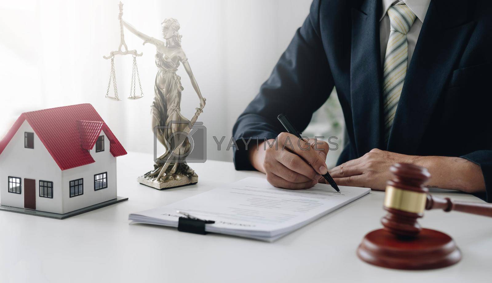 Royalty free image of Judge gavel and house model on the table. Man signing in document. Real Estate Lawyer by wichayada