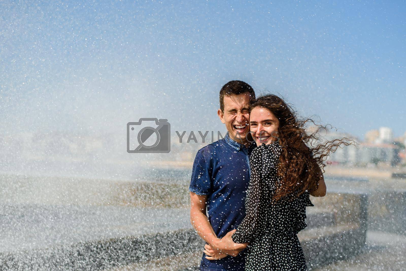 Splashing a wave of the ocean on two people in love. Lifestyle of couple. Having fun and laughs. Porto, Portugal, near Atlantic ocean.