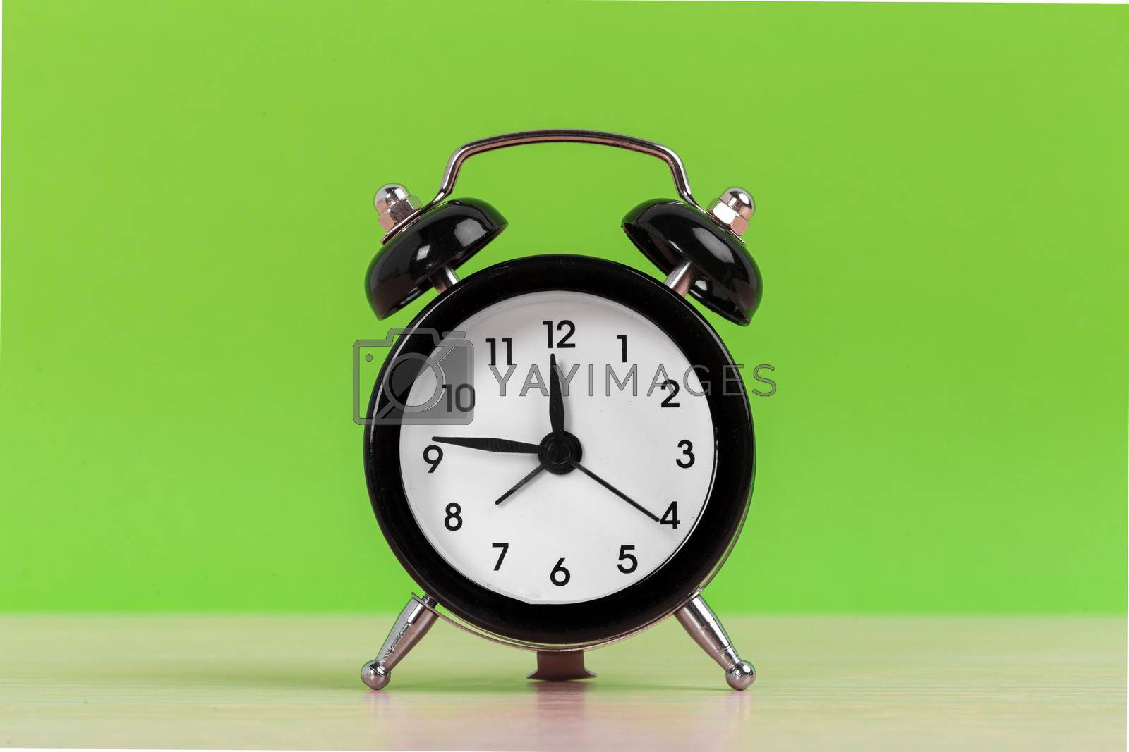Royalty free image of Vintage black alarm clock on a bright green background by Fabrikasimf