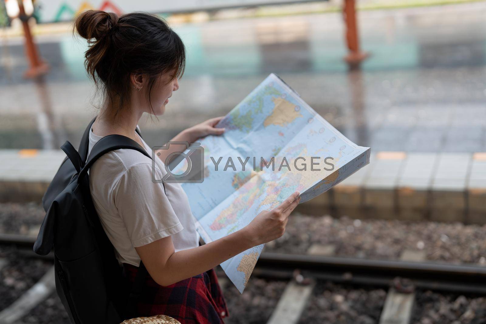 A young woman traveler standing with map choose where to travel and bag waiting for train at train station.