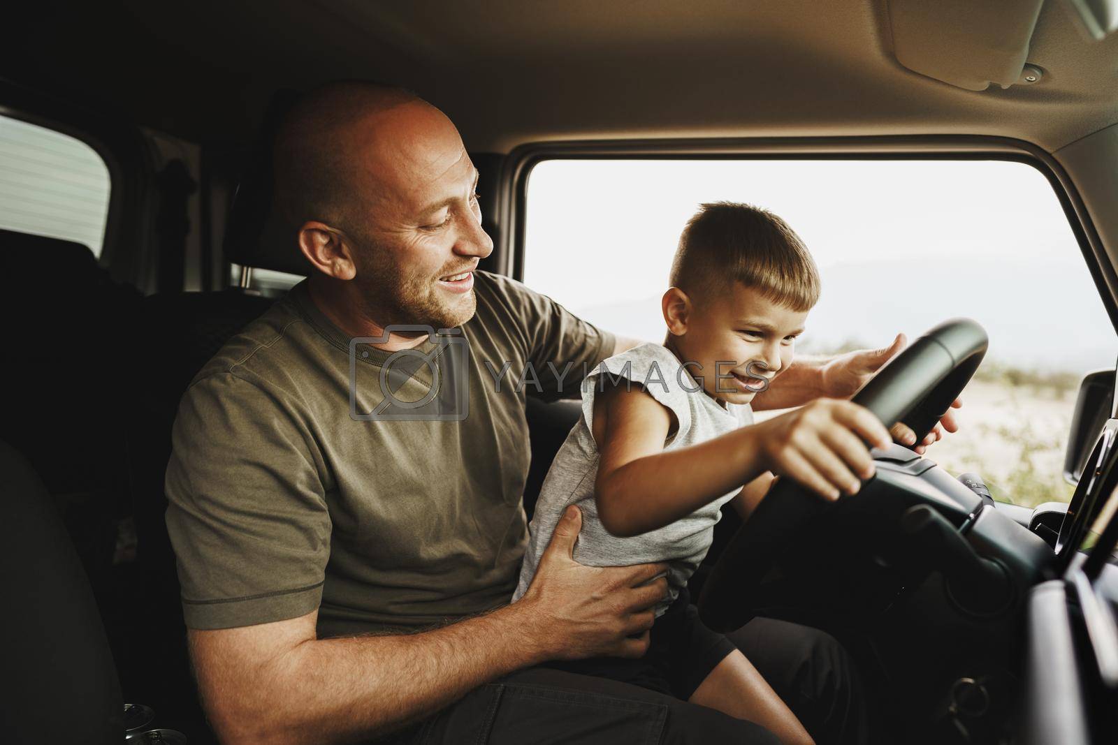 Father teaches little son to drive on road trip, close up