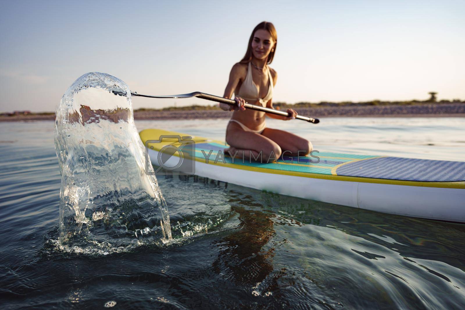 Royalty free image of Close up of young woman sitting on a stand up paddle board by Fabrikasimf