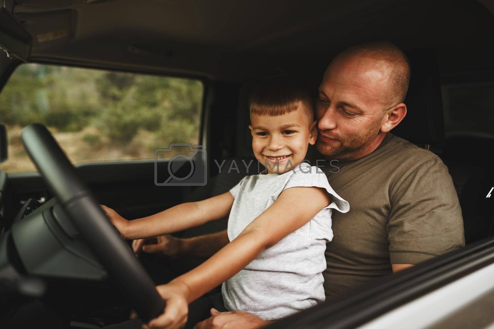 Father teaches little son to drive on road trip, close up