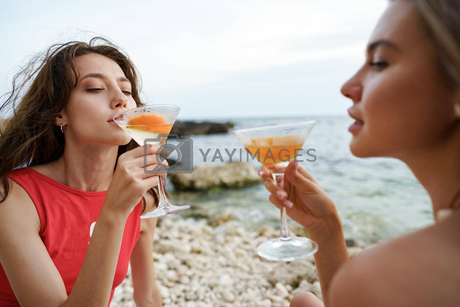 Royalty free image of Two young female friends having picnic on a beach drinking cocktails by Fabrikasimf