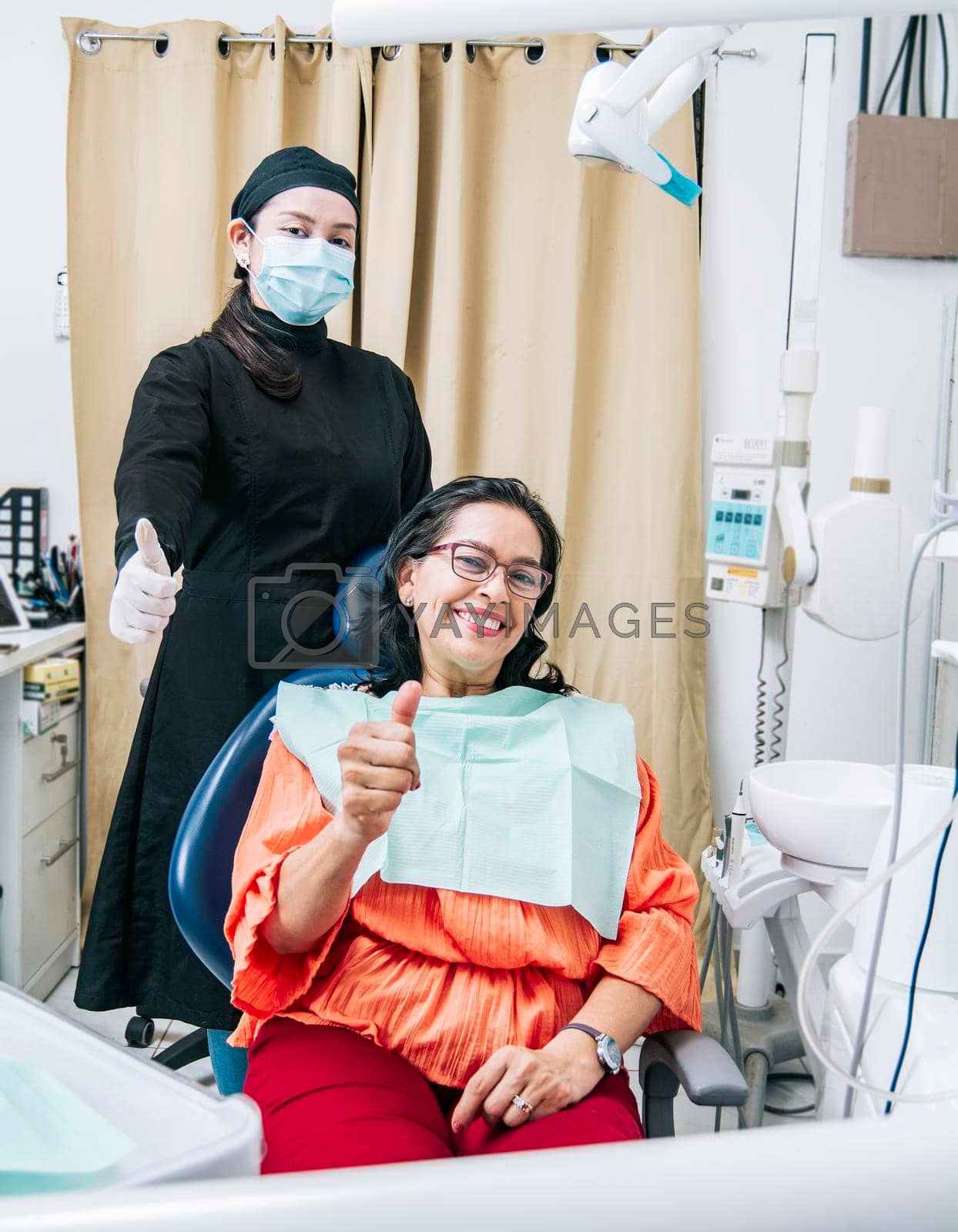 Dentist with thumb up patient in office, Woman shows thumb up sitting in dentist office, Dentist and satisfied patient with thumb up