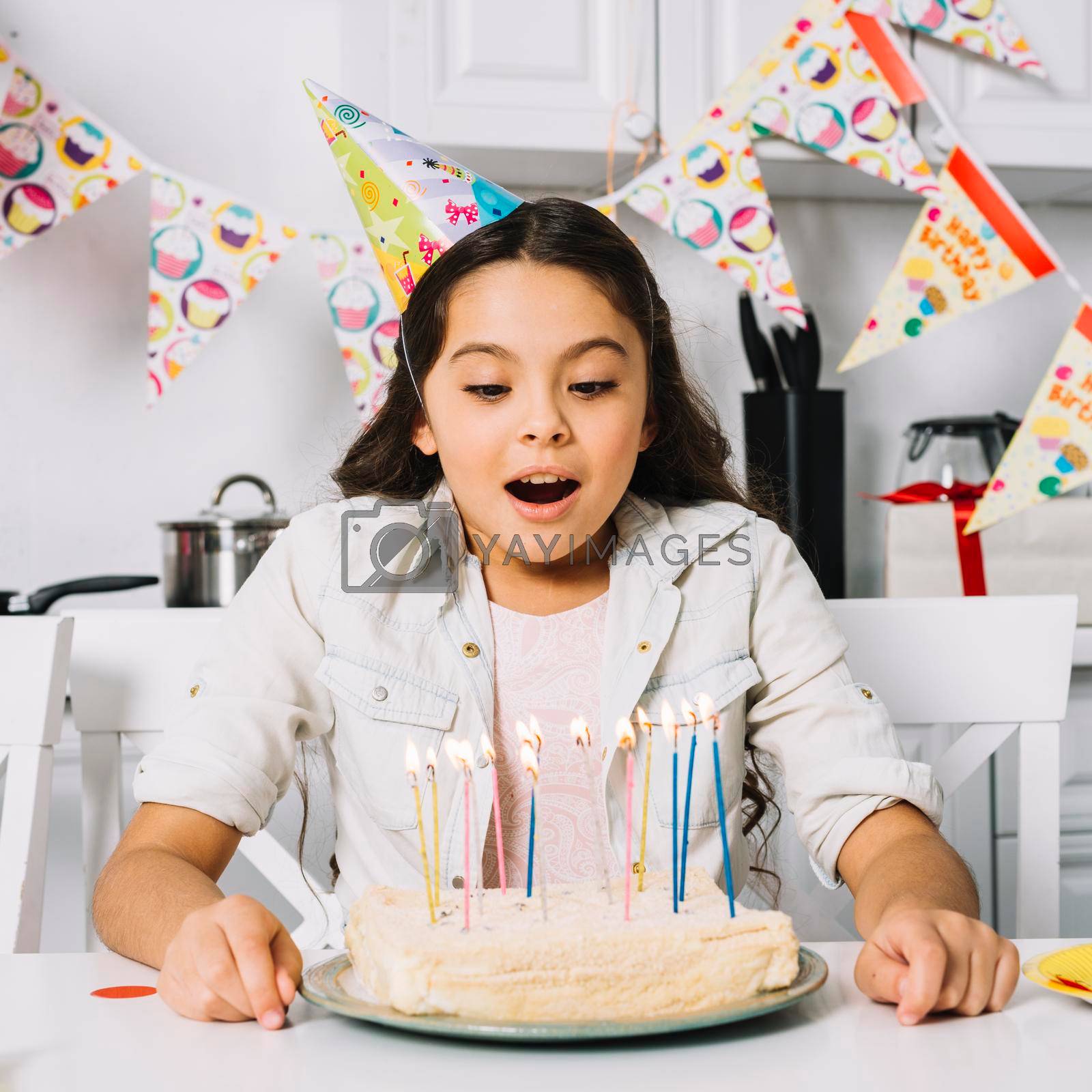 Royalty free image of surprised birthday girl blowing cake with illuminated candles by Zahard