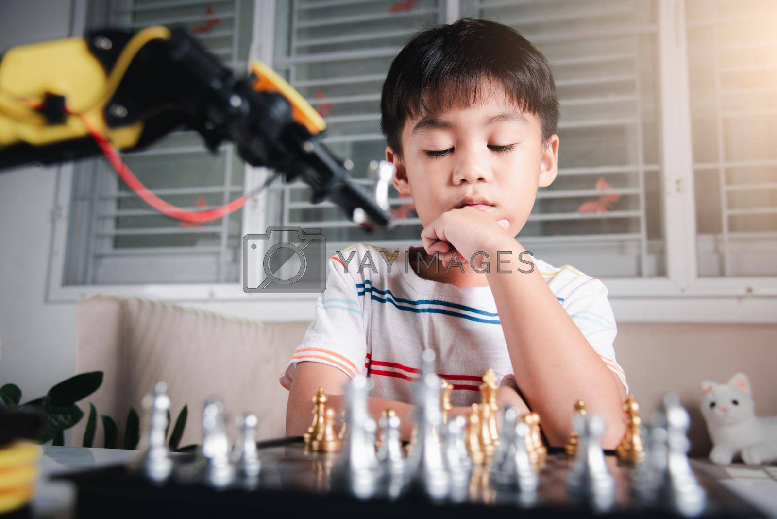Royalty free image of Asian little boy thinking and wait robot arm playing chess by Sorapop