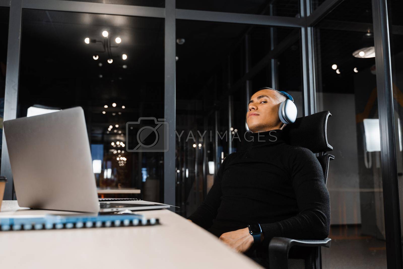 Royalty free image of Overtime working. Asian man with closed eyes is resting at work at laptop. Tired male programmer taking a break due to overtime work by Rabizo