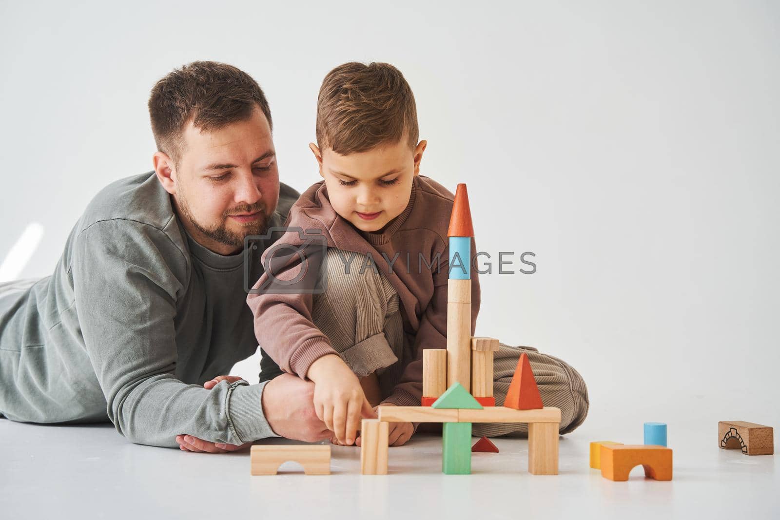 Royalty free image of Paternity. Son and dad playing with colored bricks toy on white background. Father takes care of his kid. by Rabizo