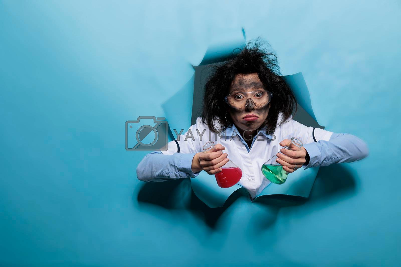 Royalty free image of Insane chemist with silly facial expression holding glass jars filled with experimental liquid serum while looking at camera. by DCStudio