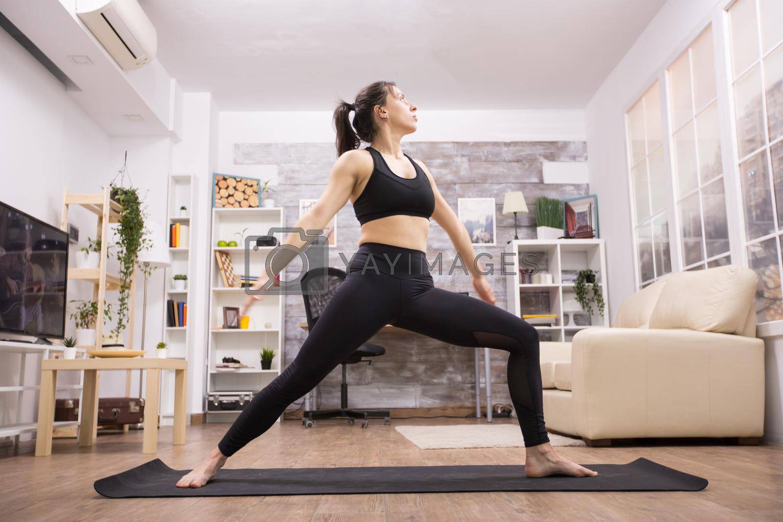 Beautiful brunette standing in warrior yoga position wearing black sportswear in living room.
