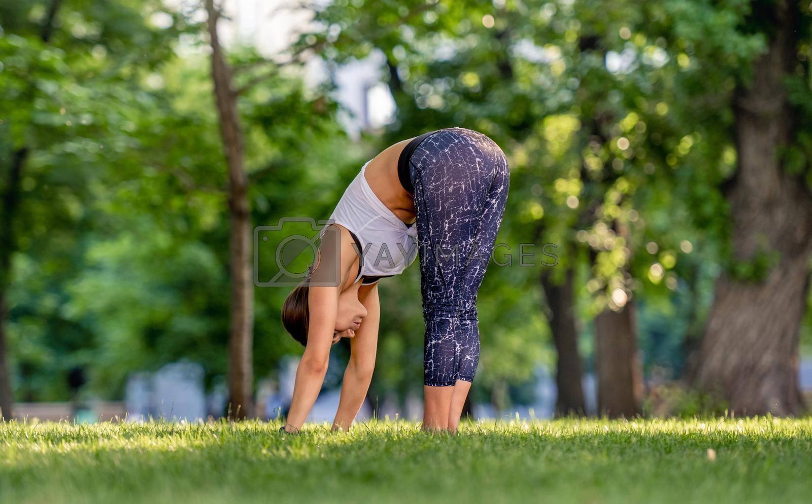 Girl doing yoga at nature and holding her body down Young woman stretching her back and legs in summertime outdoors