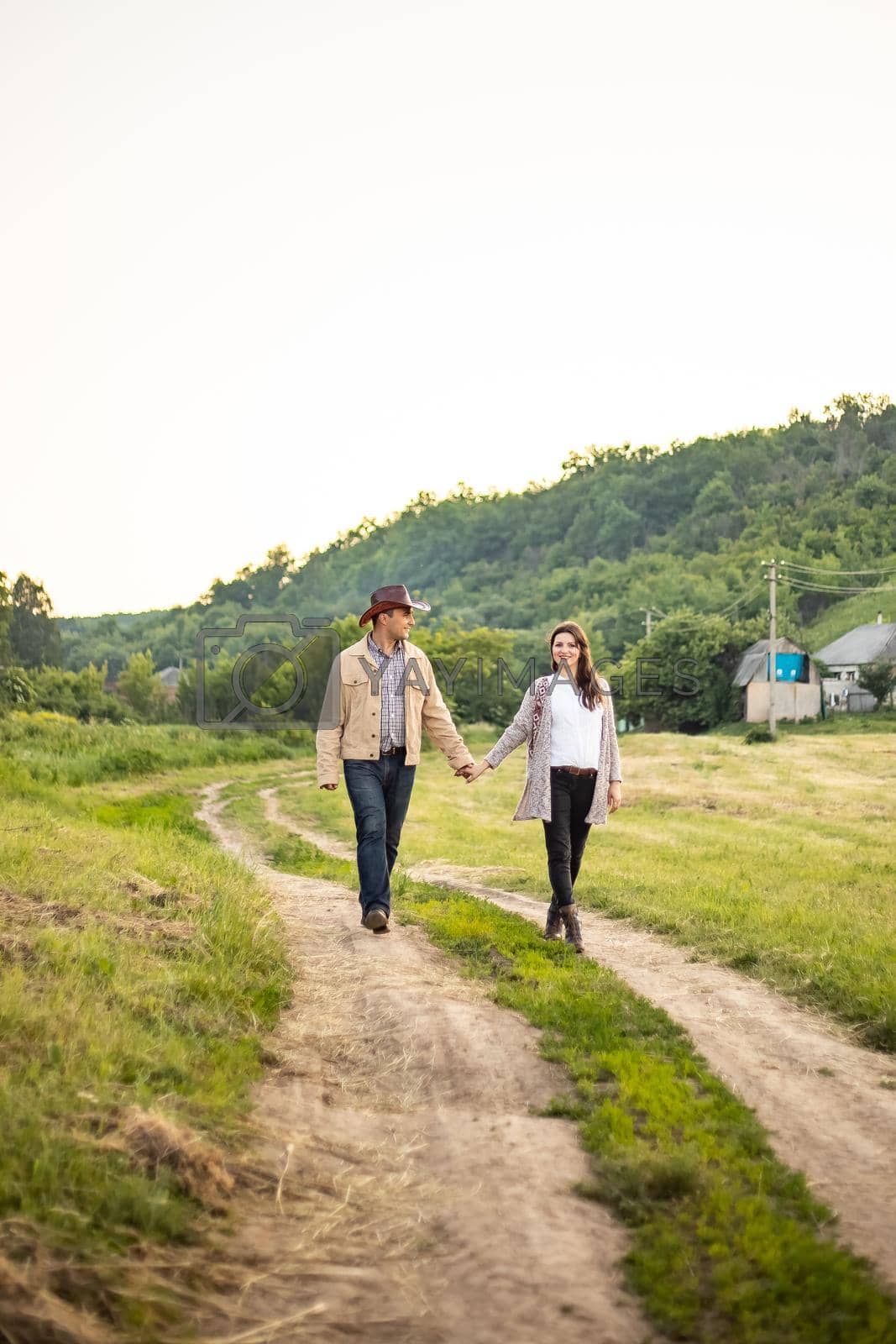 Royalty free image of A Caucasian heterosexual couple walks down the alley, holding hands, near a picturesque village in Ukraine. Vertical photo. by Anyatachka